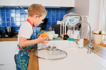 a boy in an apron washes dishes in the kitchen at home.