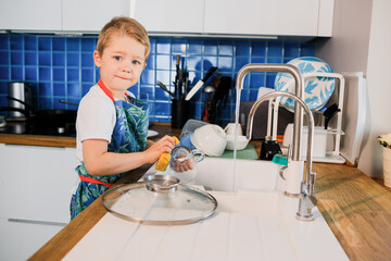 a boy in an apron washes dishes in the kitchen at home.