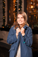 Excited girl wearing a coat on a cold weather on holidays outdoors near a decorated cafe or restaurant.