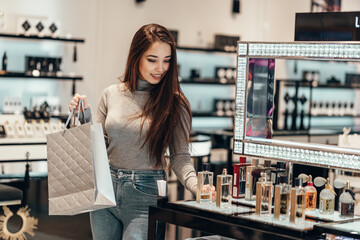 Happy beautiful Asian girl smiling young girl buys perfume cosmetics in the store - obrazy, fototapety, plakaty