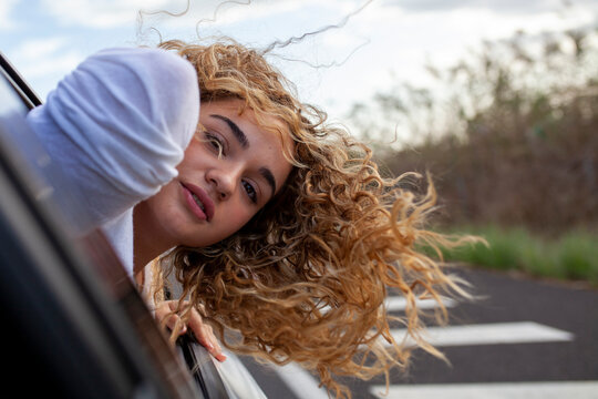 Chica joven de pelo rizado asomando la cabeza por la ventanilla