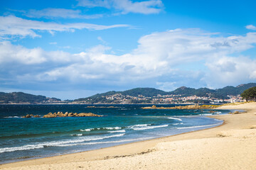 Spain Vigo Praia do Vao beach water waves blue water sky clouds hills mountains Playa de Calzoa...
