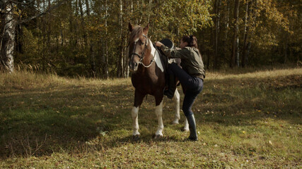 A young girl in the autumn near the stable sits on a horse on horseback and goes for a walk at a...