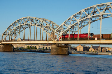 Red train crossing railway bridge over river Daugava