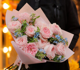 Young woman florist holding big beautiful blossoming bouquet of pink roses and blue oxypetalum flowers.