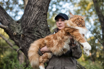 A woman holding in arms a huge maine coon cat in forest in fall.