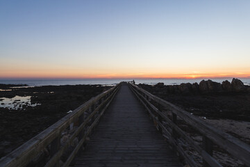 Fototapeta premium Praia do Coral sunset Viana do Castelo Portugal shore coast beach rocks sand footbridge pathway wooden blue violet sky
