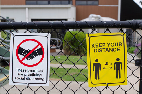 The signs with the text 'These Premises Are Practicing Social Distancing' and 'Keep Your distance 1.5m' on the metal fence outside a building. Prevention measures of coronavirus pandemic in public.