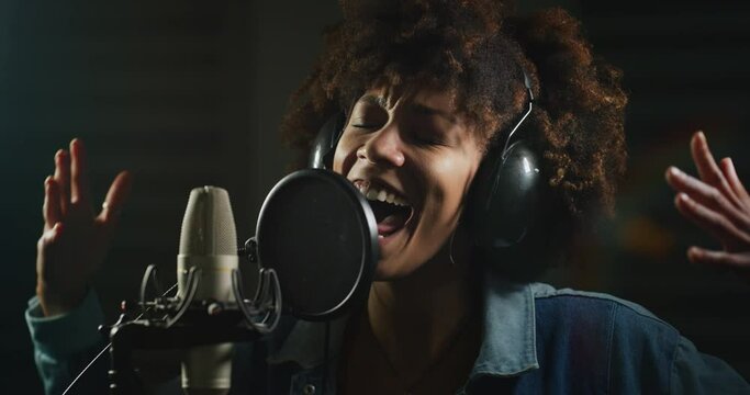 Cinematic shot of young professional african female singer is performing a new song with a microphone while recording it in a music studio. Concept of arts, love and passion for music.