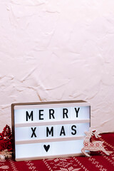Small lightbox on white concrete and red christmas patterned background. Wooden Christmas toys.
