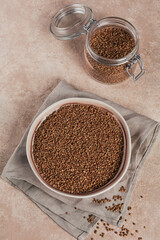 Bowl of dry raw buckwheat groats and glass jar on a light beige background. Cooking buckwheat porridge concept.