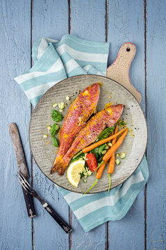 Traditional mediterranean barbecue red mullet with vegetable served as top view on a design plate