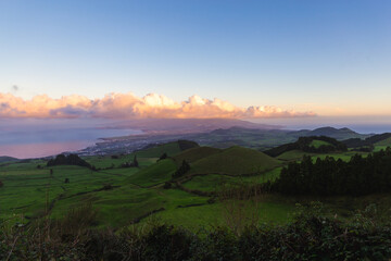Sao Miguel island Portugal sunset over blue sky violet clouds green fields hills city ocean shore Ponta Delgada summer evening