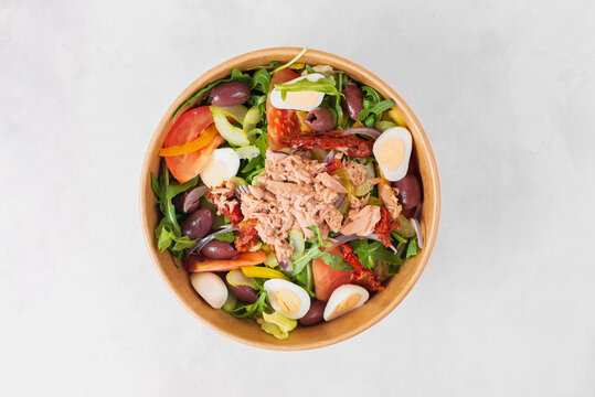 Fish diet salad with tuna, tomatoes, arugula on light background top view. Healthy lunch. Eco-friendly carton packaging, environment protection. Food delivery in disposable plate of craft paper.