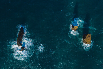 drone shot look view from above of an ocean waves crushing into the rocks island blue water sunny day 