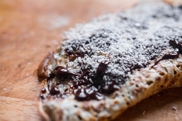 Delicious typical french crepe with melted chocolate and coconut powder. Homemade cuisine. Macro close up.