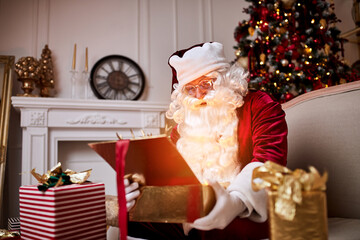 Surprised Santa Claus with a magical glowing gift near beautiful christmas tree.  New year and Merry Christmas , happy holidays concept