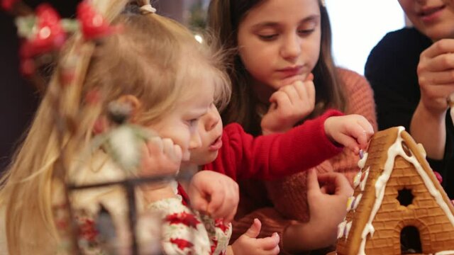 Happy Family, During Christmas Time Decorating Gingerbread House, Stay Home activity, December 2020, 3 Cute sisters cover cookies with Frosting and Sugar, Best Family Traditions 