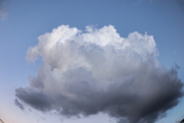 large white cumulus cloud shaded in various shades of gray, floating isolated in a sky in pastel color.