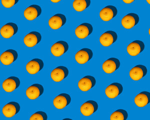 Fototapeta premium A pattern of little bright orange mandarins with a pronounced shadow on a bright blue background. Mandarin set, healthy food.