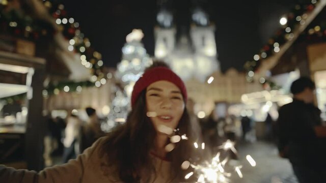 Selfie time, girl blogger is making video and photo for her social page at the street fair on the central Square of Prague. Gorgeous Asian smiling and burning bright sparklers on New Year's Eve.