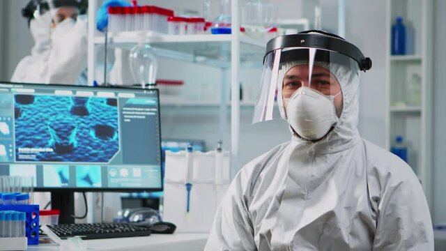 Tired doctor in protection suit against covid-19 looking exhausted at camera in equipped lab. Team of scientists examining virus evolution using high tech for scientific research, vaccine development.