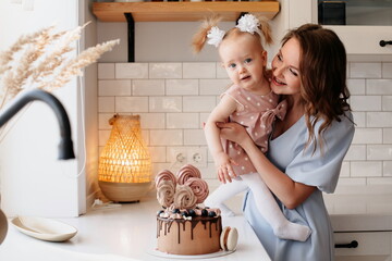 beautiful woman holds in her arms a little girl near the birthday cake. portrait of mom and...