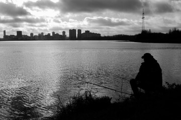 Horizontal conceptual monochrome photography with silhouette of a fisherman on the foreground and city skyline on the background