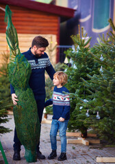 happy father and son buying a real lush christmas tree on a christmas market during winter holidays