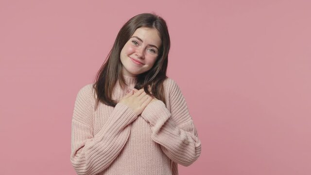 Amazed smiling young woman 20s years old in casual pastel sweater posing isolated on pink color background in studio. People lifestyle concept. Looking camera put hands folded on heart waving hands