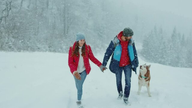 Happy couple man and woman have fun walking with husky in winter forest playing and throwing snow. Smiling frost outside. Dog. Christmas winter holiday. Slow motion