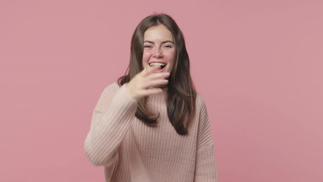 Excited laughing cheerful brunette young woman 20s years old wearing casual pastel sweater posing isolated on pink color background in studio. People lifestyle concept. Pointing index finger on camera