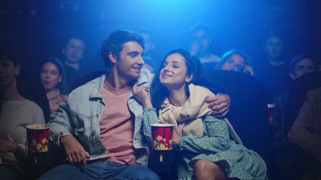 Happy couple watching movie in cinema. Happy man kissing woman in dark hall.