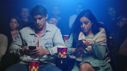 Upset man and frustrated woman looking in cellphones in movie theater.
