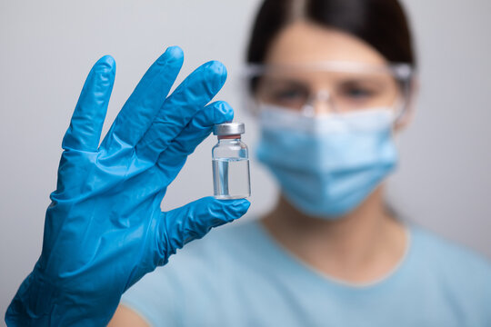 Doctor scientis in protective gloves and mask holding glass vial with injection liquid. Vaccination against influenza and coronavirus.