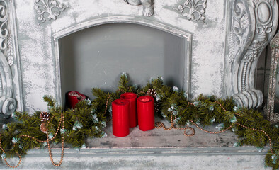 Fototapeta na wymiar decoration of a gray fireplace with red candles and Christmas tree branches, patterned decoration of an old house, New Year's concept