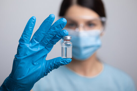 Doctor scientis in protective gloves and mask holding glass vial with injection liquid. Vaccination against influenza and coronavirus.
