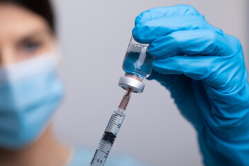 Doctor scientis in protective gloves and mask holding glass vial with injection liquid. Vaccination against influenza and coronavirus.