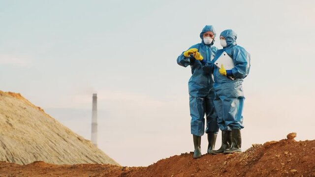 Full shot of ecologists in costumes and masks discussing orange soil of isolated landscape with hazardous ecology