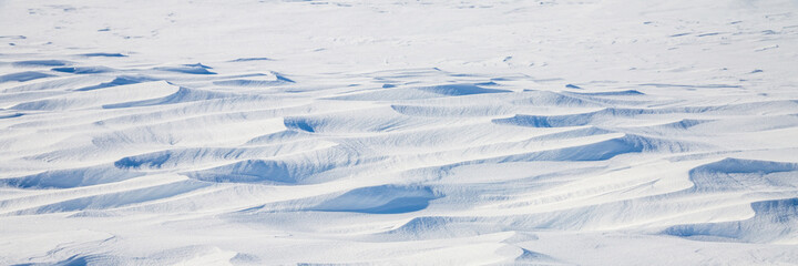Fototapeta na wymiar Snow texture. Wind sculpted patterns on snow surface. Wind in the tundra and in the mountains on the surface of the snow sculpts patterns and ridges. Arctic, Polar region. Winter panoramic background.