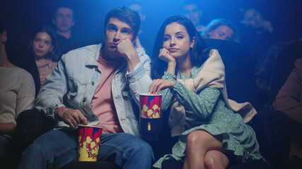 Upset couple eating popcorn in cinema. Frustrated people looking movie in hall.