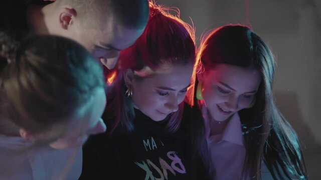 Group of teenagers watching footage of them roller skating on camera. Girl holding video camera in hands checking recording of friends doing tricks and pulling dance moves. Concept of youth, nightlife