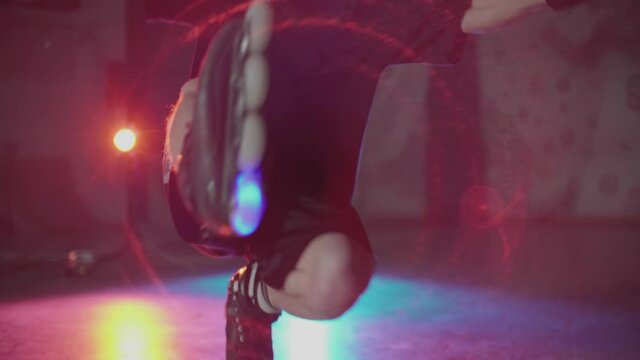 Young guy roller skating on one leg on spotlight. Teenager showing impressive skills freeskating and active nightlife lifestyle of extreme sport. in dark studio. Concept of youth, subculture.