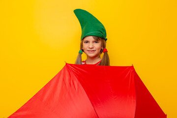 Little girl dressed as Christmas elf hiding behind an umbrella