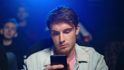 Busy man looking mobile phone in cinema. Bored guy watching film in dark hall.