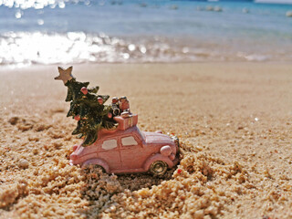 Fototapeta na wymiar Pink car drives a Christmas tree on the beach