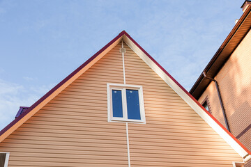 The facade of the new house clad with siding, with windows, against the blue sky.