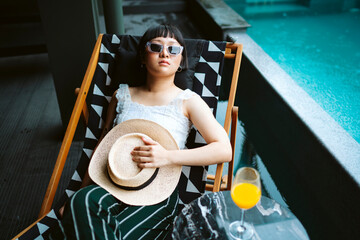 Fototapeta na wymiar Asian woman wearing sunglasses and hat laying on beach chair in hotel.