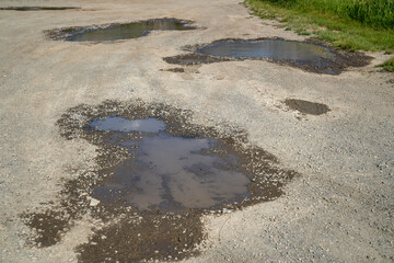 Obraz premium Potholes on a gravel dirt road, filled with water