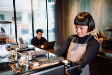 Fototapeta na wymiar Asian woman working as barista making coffee for customer in cafeteria.